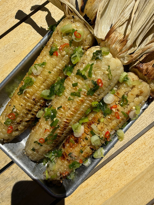 Charred Vietnamese grilled corn on the cob brushed with caramelized fish sauce glaze and topped with green scallion oil, served on a sheet pan or platter.