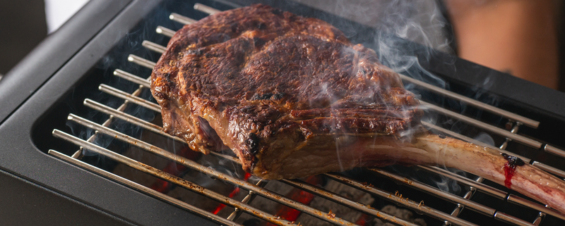 Thick tomahawk steak with a dark seared crust laying on the Thaan Grill
